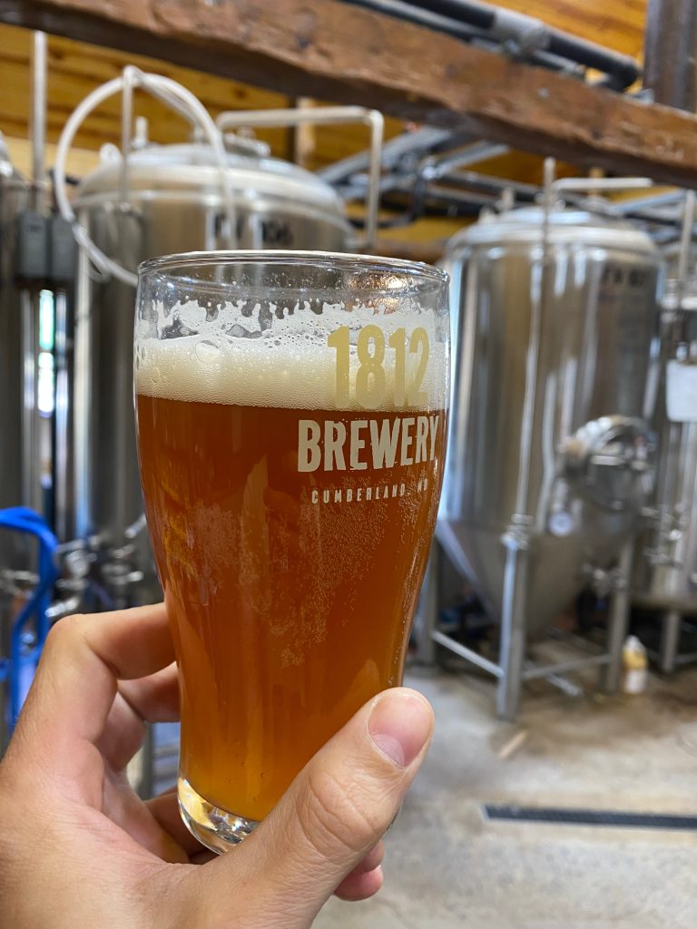 The Brewer holding a tasting glass in front of the brewing tanks.